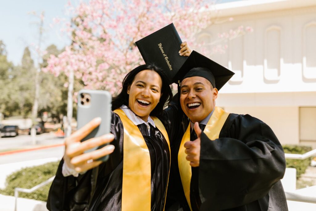 Two smiling graduates in caps and gowns taking a selfie
