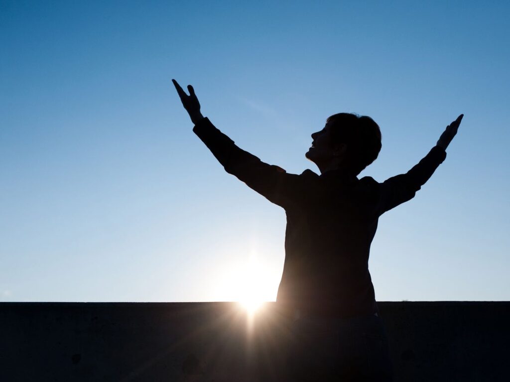 Silhouette of a person raising their arms toward the sunrise, a symbol of freedom